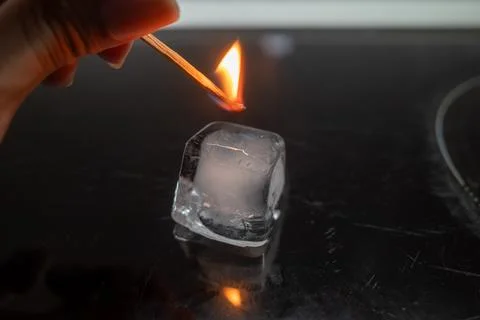Hand ignites ice cube with match flame Photos