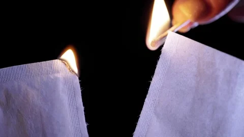 Hand Igniting Torn Paper Packets With Lit Match Against Black Background 库存影片 330301821
