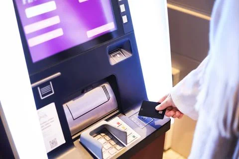Hand inserting a black debit card into an ATM cash machine with a glowing p.. Stock Photos