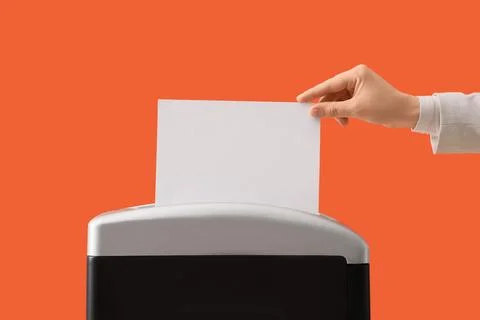 Hand inserting a blank white paper sheet into a document shredder for destruc Stock Photos