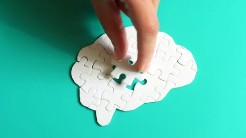 Hand Inserting Puzzle Piece into a Brain Shape on Teal Surface Video stock 295111303