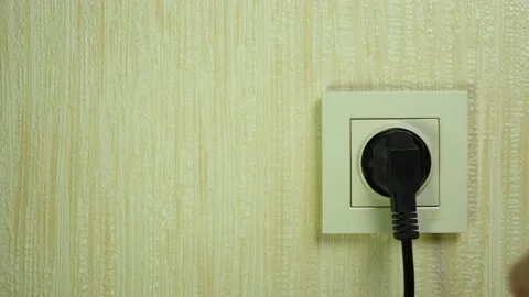A hand inserts a black electric plug into a white plastic socket on the wall Stock Footage 231421786