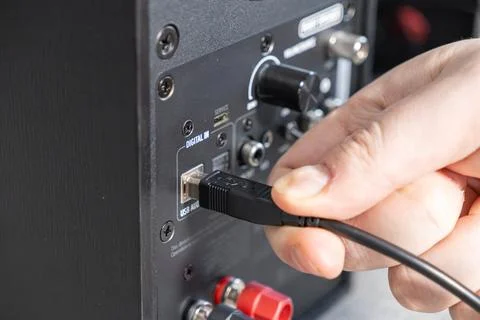 A hand inserts a black USB cable into the audio input port of a modern desktop 스톡 사진