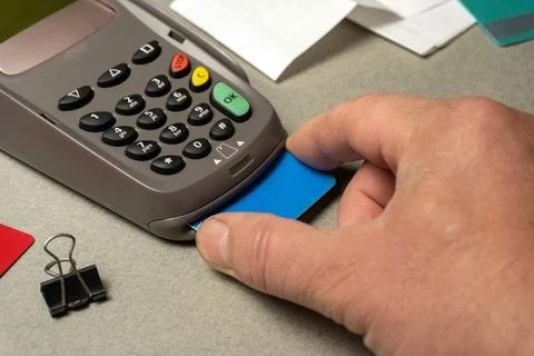 A hand inserts a card into a card reader on a gray surface. Nearby, there a.. Stock Photos