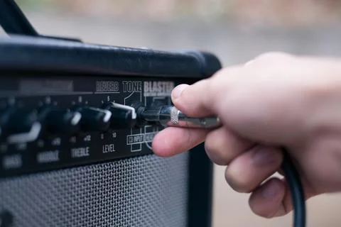 Hand inserts a cord jack into a combo amplifier for electric guitar Stock Photos