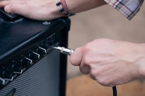 Hand inserts a cord jack into a combo amplifier for electric guitar Stock Photos