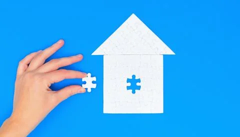 Hand Inserts Final Piece into House Puzzle on Blue Foto stock