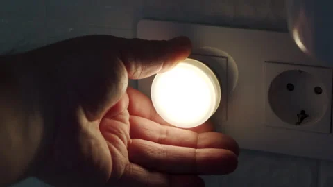 A hand inserts or removes the plastic LED night light from the wall socket. Stock Footage 320890220