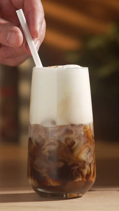 A hand inserts a straw into the drink and stirs it, blending the milk and f.. Stock Footage 335516492