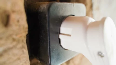 A hand inserts a white plug of an electrical appliance into an old black socket Stock Footage 198184283