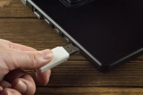 The hand inserts a white USB flash drive into the input of a black laptop, close Foto stock