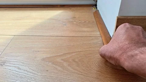 Hand Installing Floor Spacer Near Baseboard on Laminate Flooring Stock Footage 340948282