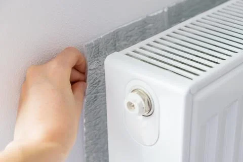 Hand installing thermal insulation behind radiator to reflect heat into the room Foto stock