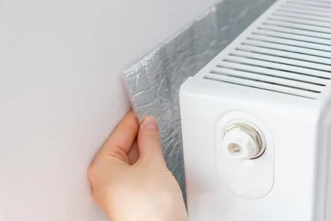 Hand installing thermal insulation behind radiator to reflect heat into the room Stock Photos