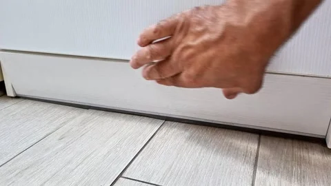 Hand Installing a White Baseboard Trim Along the Bottom of Furniture on Floor Vidéo 346802526