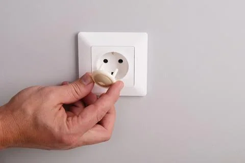 A hand installs a protective plug into an electrical outlet to protect childr 스톡 사진