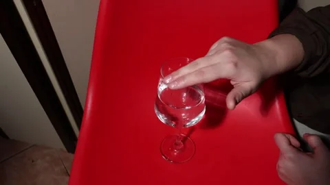 Hand interacting with a glass of water on a red surface Stock Footage 339180004