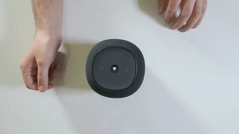 Hand interacting with a smart speaker, adjusting the volume on a white Stock Footage 296848798