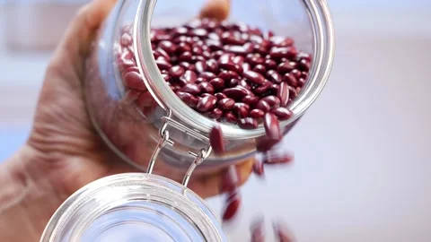 A hand with a jar of red beans. Red beans in a jar. Pouring beans into a glass 動画素材 248434264