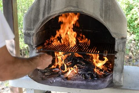 Hand keeps fire going in a grill with fiery flames - an empty fire grate Stock Photos