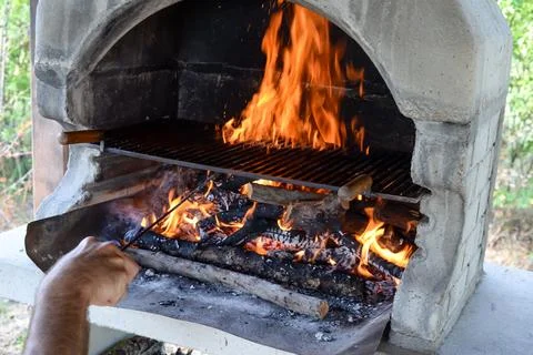 Hand keeps fire going in a grill with fiery flames - an empty fire grate Stock Photos