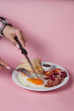 Hand with knife and fork cuts breakfast, scrambled eggs with tomatoes and toast Stock Photos