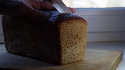 A hand with a knife carefully cuts the first piece of fresh, soft black bread Stock Footage 331832114