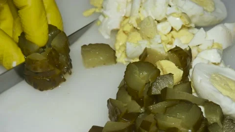 A hand with a knife cuts a pickled cucumber,  next to boiled eggs, on a cutt 스톡 동영상 229593505