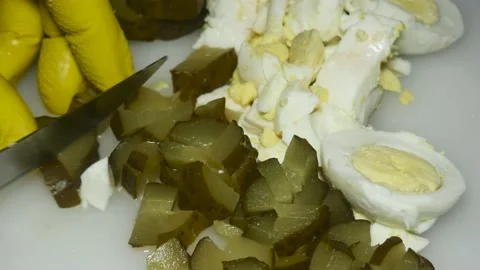 A hand with a knife cuts a pickled cucumber, close-up, next to boiled eggs, Vidéo 229593533