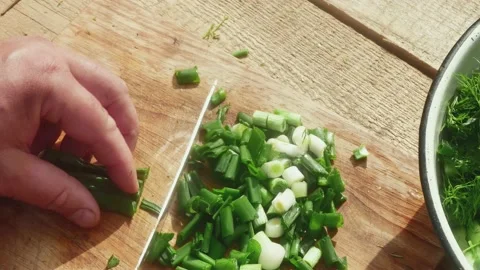 A hand with a knife cuts a spring leek on a wooden board for a spring salad 스톡 동영상 190585252
