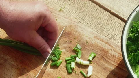 A hand with a knife cuts a spring leek on a wooden table, close-up Vídeos de archivo 190586370