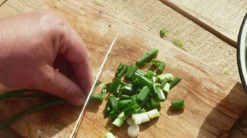 A hand with a knife cuts a spring leek on a wooden table Vídeos de archivo 190586415