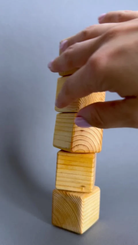 Hand knocking down wooden block tower against gray background. The video represe Stock Footage 339696598