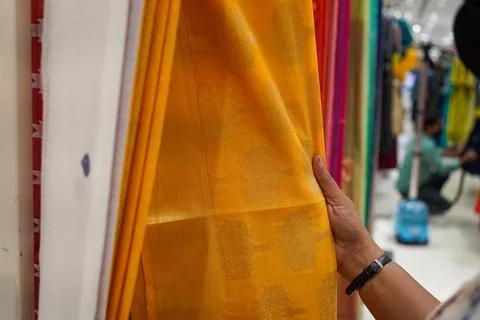 Hand of a lady selecting yellow colored saree in a shop Stock Photos