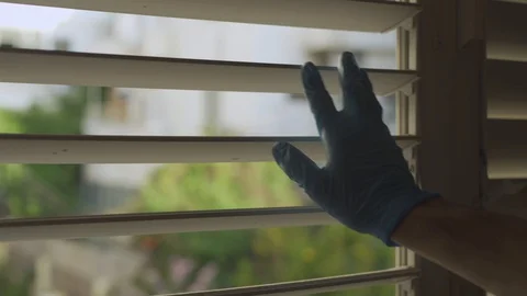 Hand with latex glove opens window shutters to look outside and closes them shut Stock Footage 128840379
