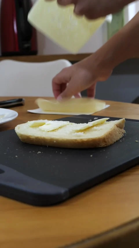 Hand laying cheese slice on buttered bread at home kitchen table Stock Footage 342643520