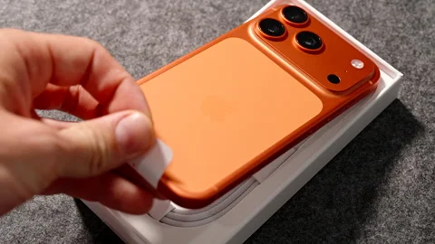 Hand Lifting Cosmic Orange iPhone 17 Pro from Box Using Tab with Triple Camera Stock Footage 318057341