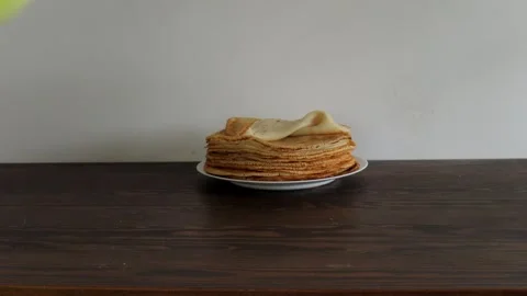 Hand lifting crepe from tall stack of thin golden pancakes on white plate over Stock Footage 309301737