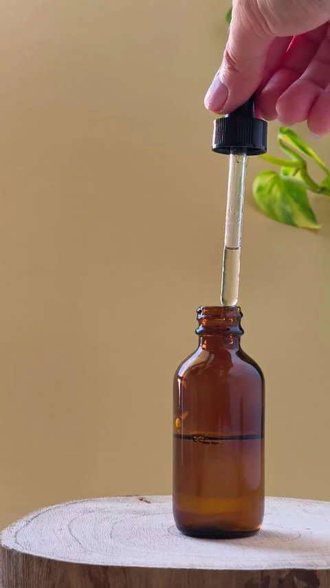 Hand lifting glass dropper with serum from amber bottle on wood. Видео 337101007