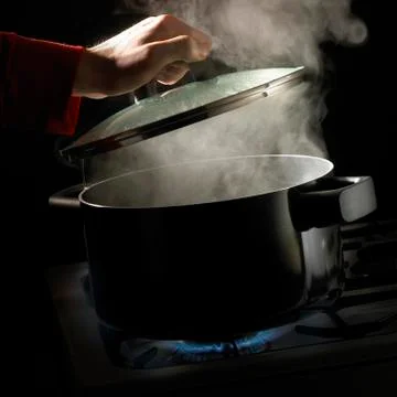 HAND LIFTING LID OFF PAN OF BOILING WATER AND RISING STEAM SIMMERING ON GAS C Stock Photos
