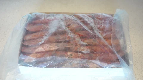 Hand lifting the paper to discover a package full of frozen Argentine prawns. Stock Footage 127798589