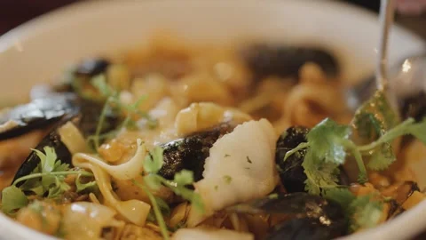 Hand Lifting Seafood Chowder Noodles with Spoon in Close-Up Stock Footage 315545979