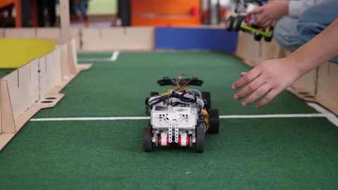 Hand lifting small wheeled robot car beside indoor turf track, with blurred Stock Footage 344872890
