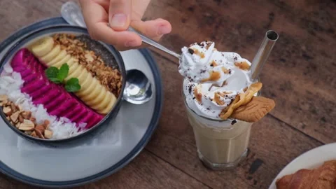 Hand lifting spoon from coffee latte decorated with whipped cream and sweets on Stock Footage 166455577