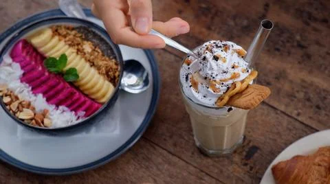 Hand lifting spoon from coffee latte decorated with whipped cream and sweets on Stock Photos