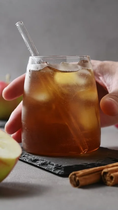 Hand lifts apple cider cold brew tonic from slate board beside fresh apples and Stock Footage 345557177