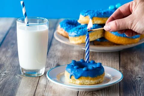 A hand lighting a candle that is inserted into a blue decorated homemade donut. Stock Photos