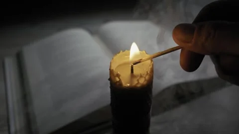 Hand Lights a Beeswax Candle with a Match in a Dark Room with a Book Stock Footage 330420206