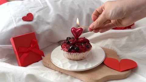 Hand lights a candle on a cake  with red Valentine decor gifts box and hearts Stock Footage 168396747