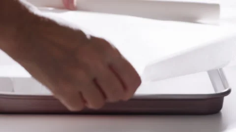 Hand lines a baking tray with parchment paper during food preparation in a kitch Stock Footage 333331031